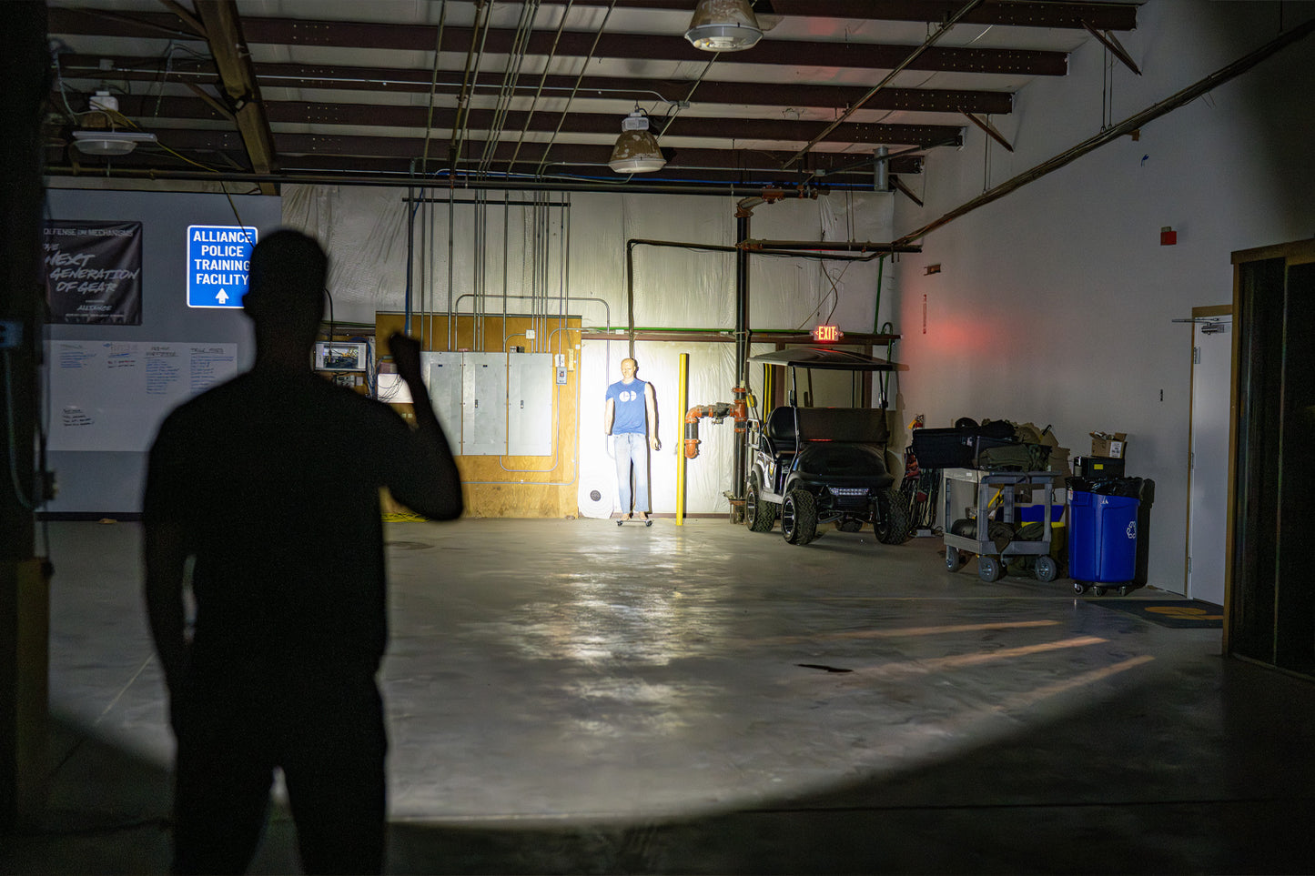 A man shining a flashlight in a garage towards a mannequin.