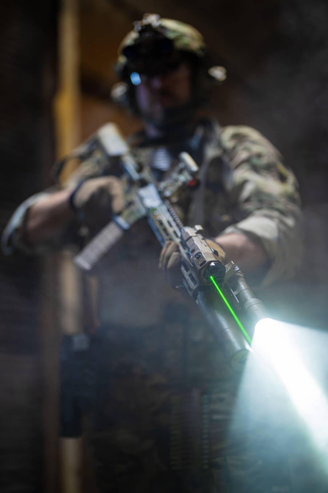 Man in tactical gear holding rifle with laser and flashlight at low ready