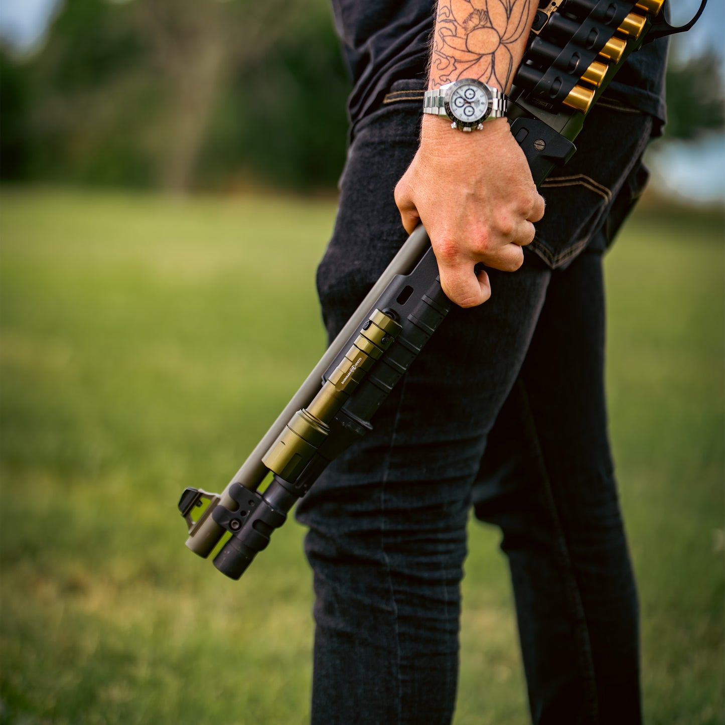 Person holding a shotgun in a grassy outdoor setting