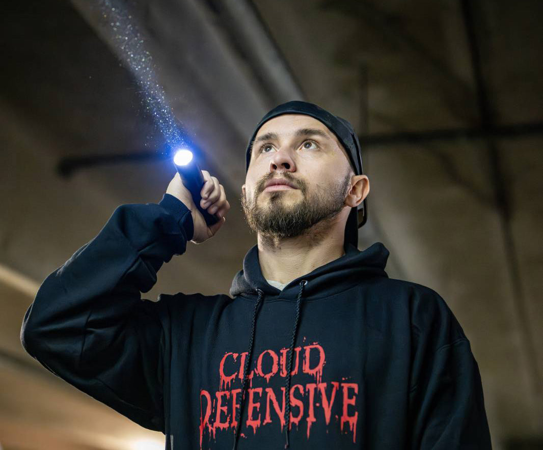 Man in a black hoodie holding a flashlight.