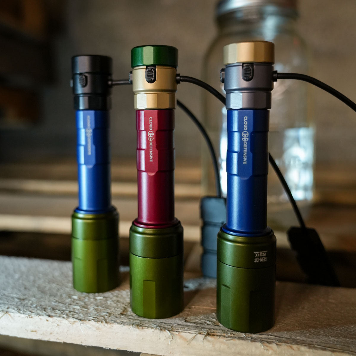 Three multi color flashlights sitting in front of a mason jar.
