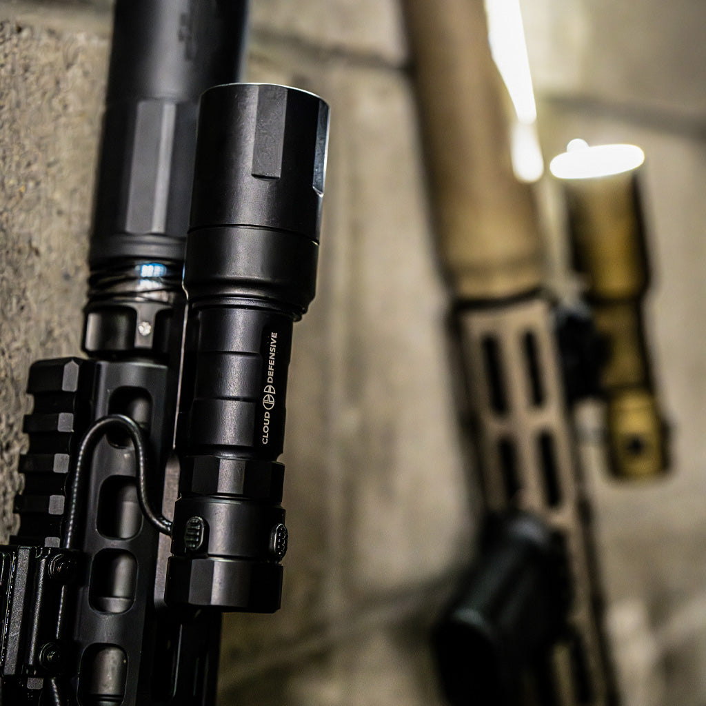 Close up of a black and a tan rifle light on two rifles.