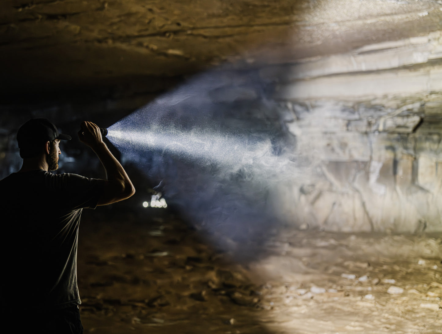 Man shining black MCH Duty flashlight into a cave. 