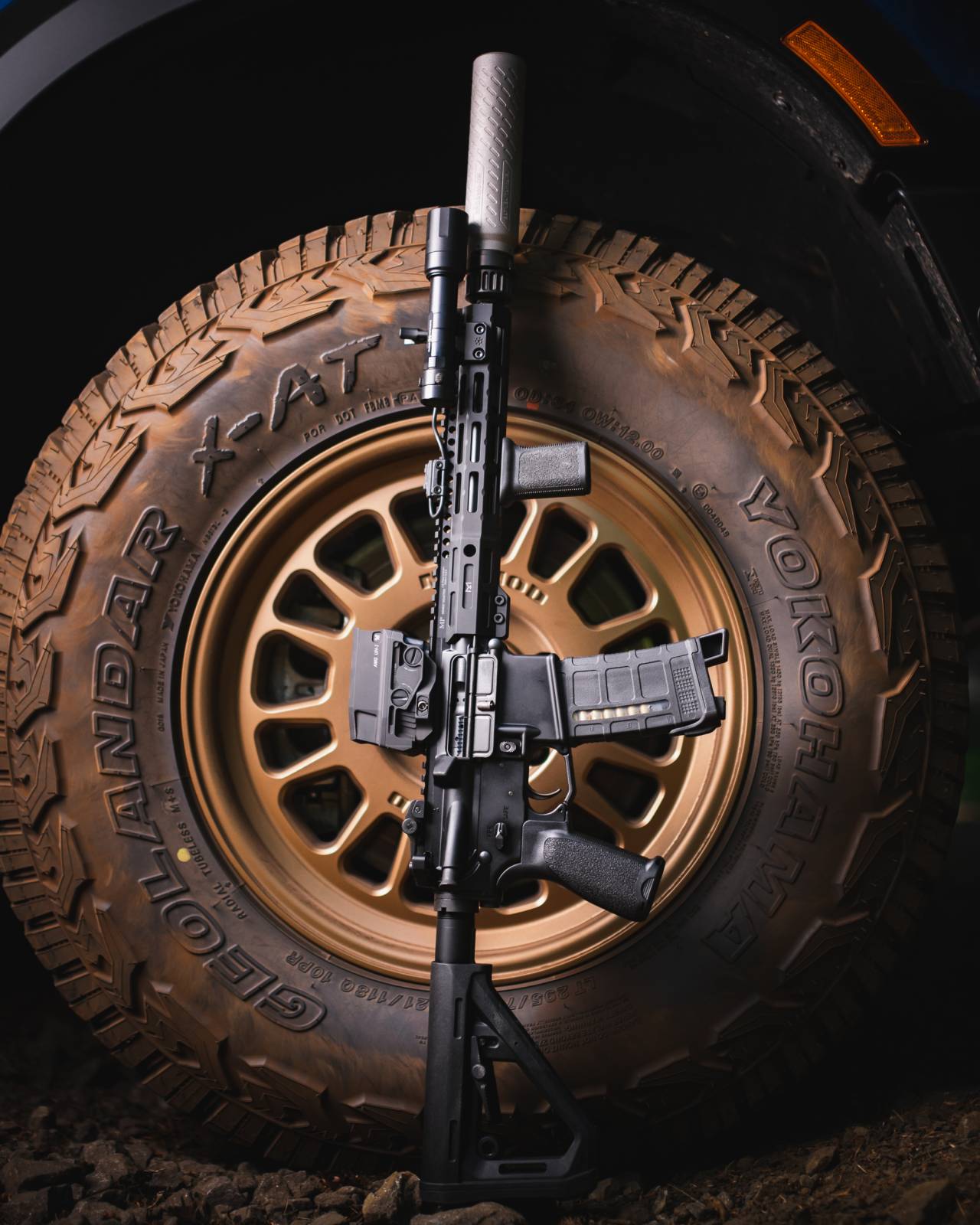 black rifle with black Rein flashlight leaning on a truck tire.