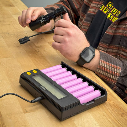 set of Samsung 30Q batteries on a charger with man holding a flashlight in the background.