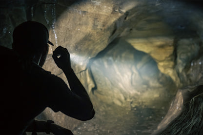 Man shining MCH Duty flashlight into a cave tunnel.