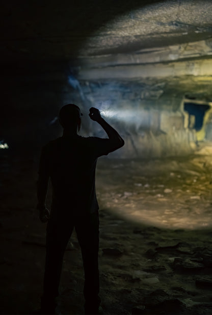 Man shining black MCH Duty flashlight into a cave from behind.