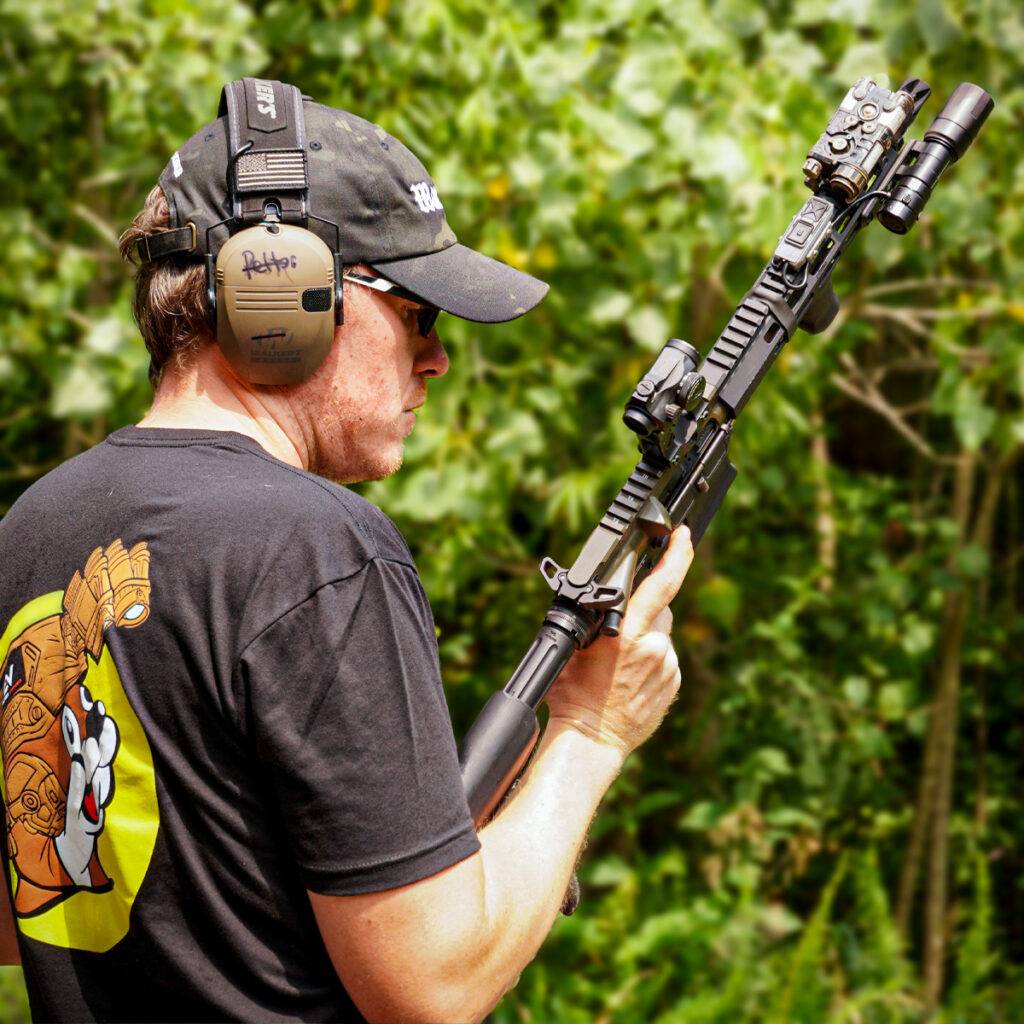 Man holding rifle with black Rein Micro flashlight mounted to it.