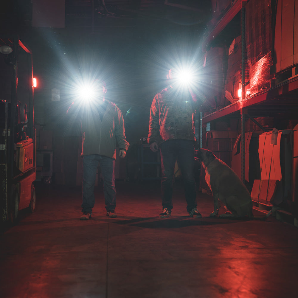 2 men in a warehouse shining MCH flashlights into the camera.